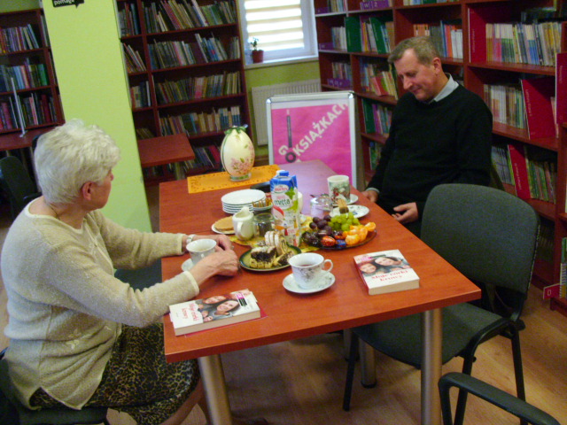 dwie osoby przy stole  z ciastem i kawą rozmawiają o książkach