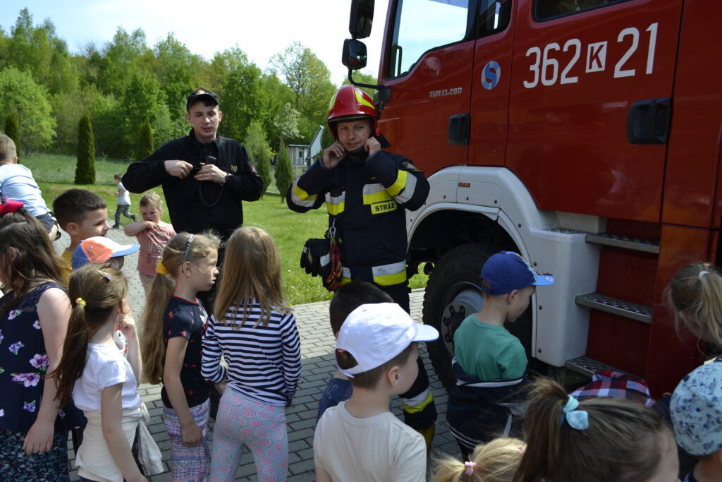 dwóch strażaków, przedszkolaki i wóz strażacki