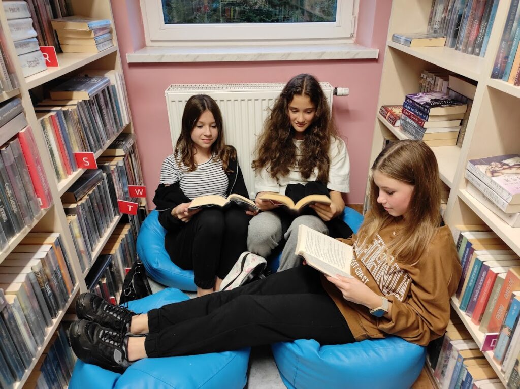 trzy osoby czytają książki w bibliotece