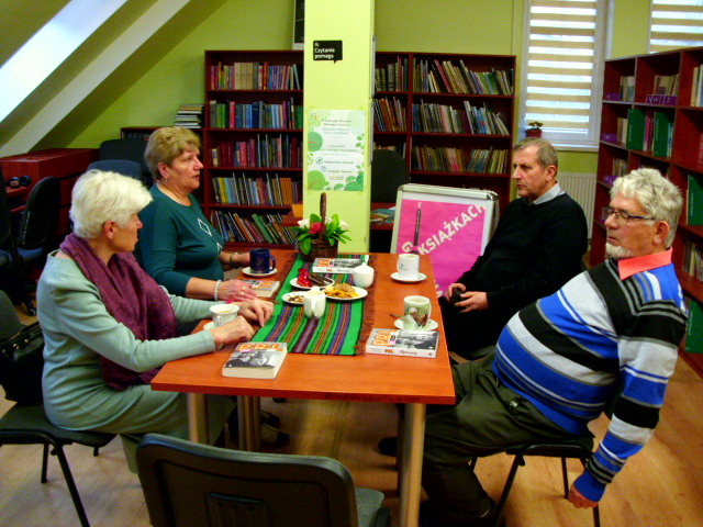 cztery osoby przy stole w bibliotece  rozmawiają o książkach