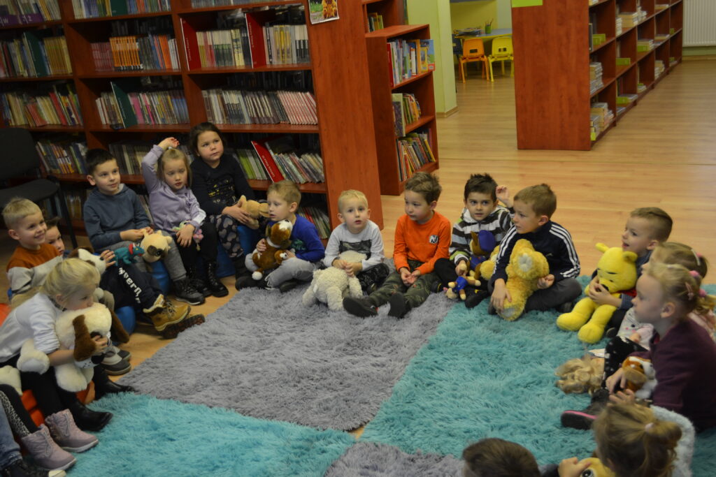 dzieci w bibliotece siedzą na dywanie i trzymają misie