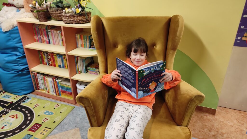 dziecko czytające książkę na fotelu w bibliotece