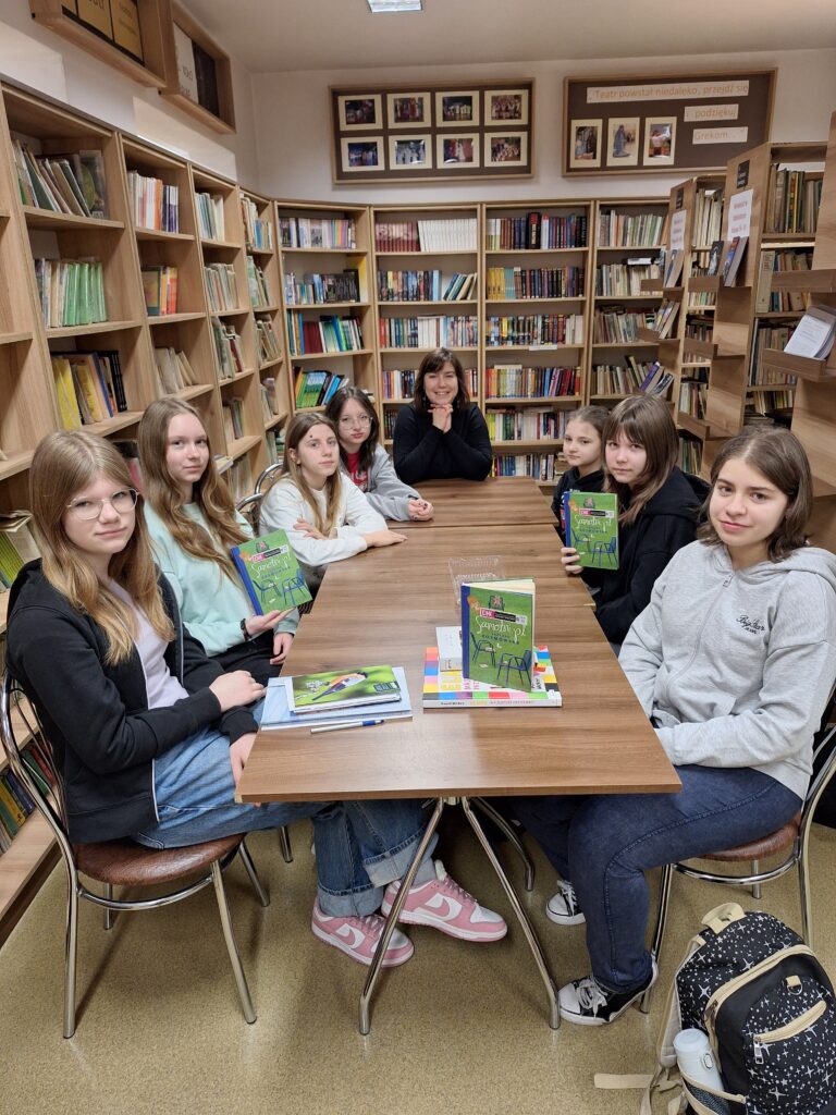 grupa osób przy stole z książkami w bibliotece