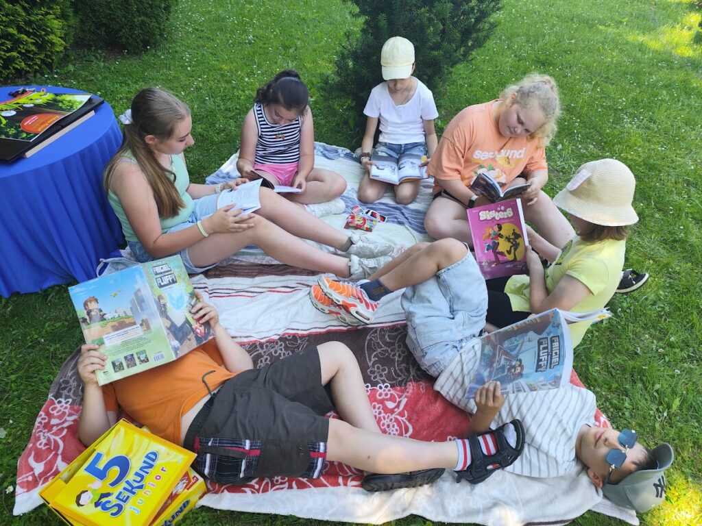 dzieci na kocyku na trawie czytają książki